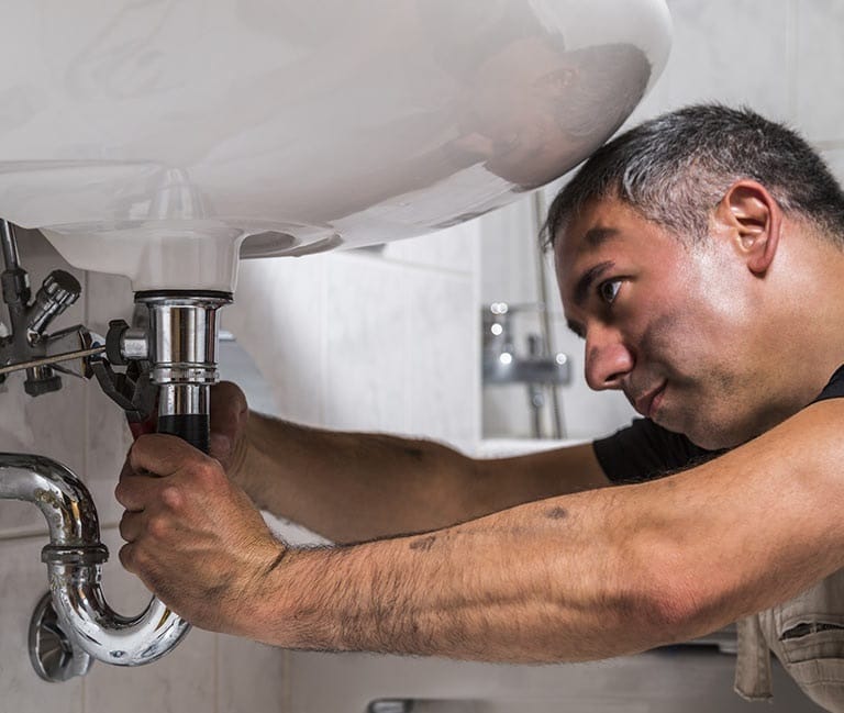 Intervention sur un siphon métallique sous un lavabo.
