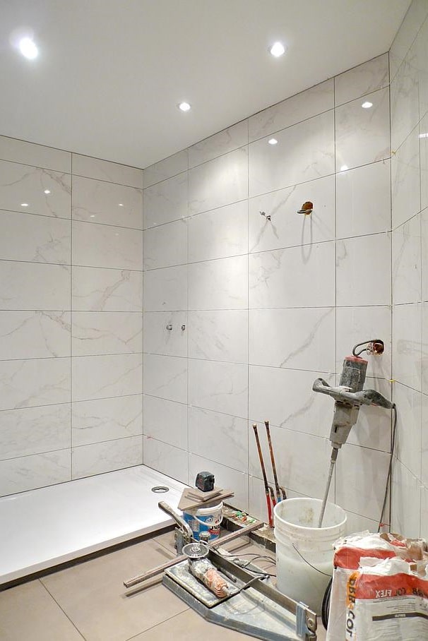Salle de bains en travaux avec baignoire, carrelage et raccordements apparents.